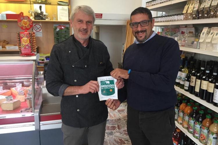 L'assessore La Malfa consegna l'adesivo dei negozi di collina a Giorgio Graziano dell'alimentari 'L Val di Vaglio